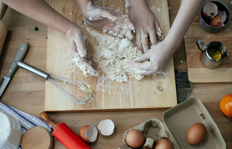 Hands kneading pasta dough on a floured wooden bench